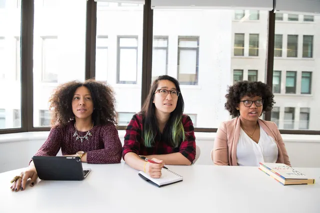 Three women discussing work around an office table.