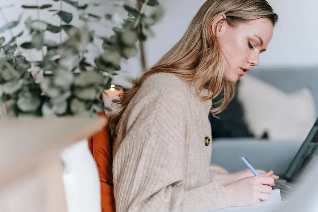 Woman writing in her planner beside her laptop.